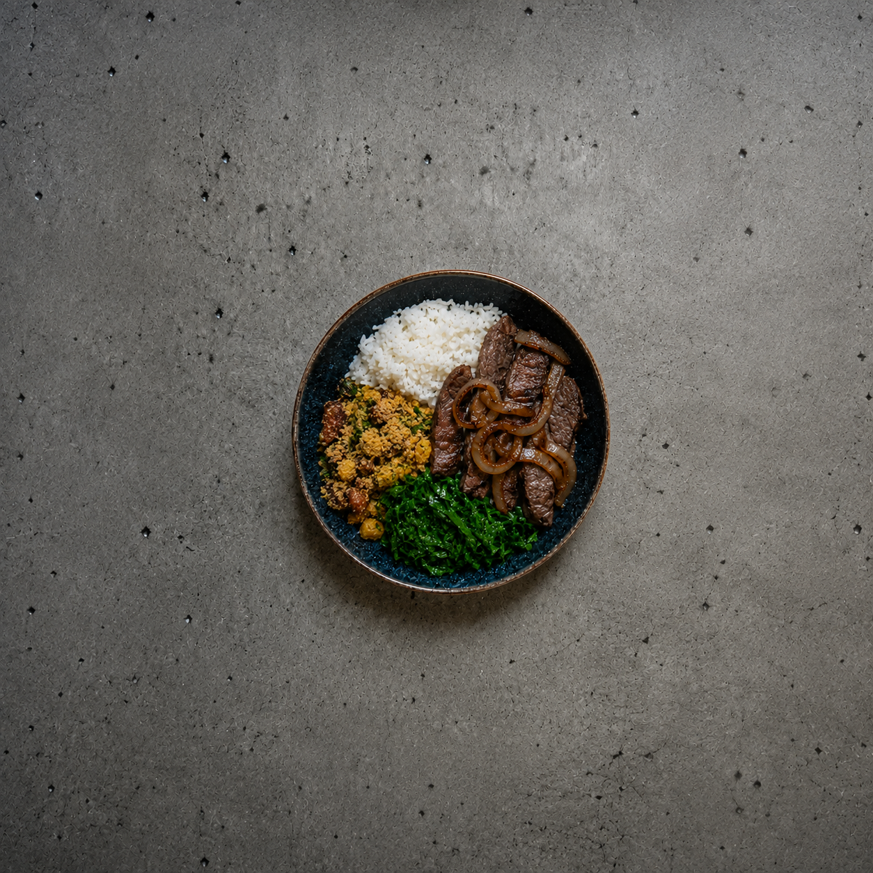 Prato com carne, arroz e acompanhamentos sobre mesa de pedra